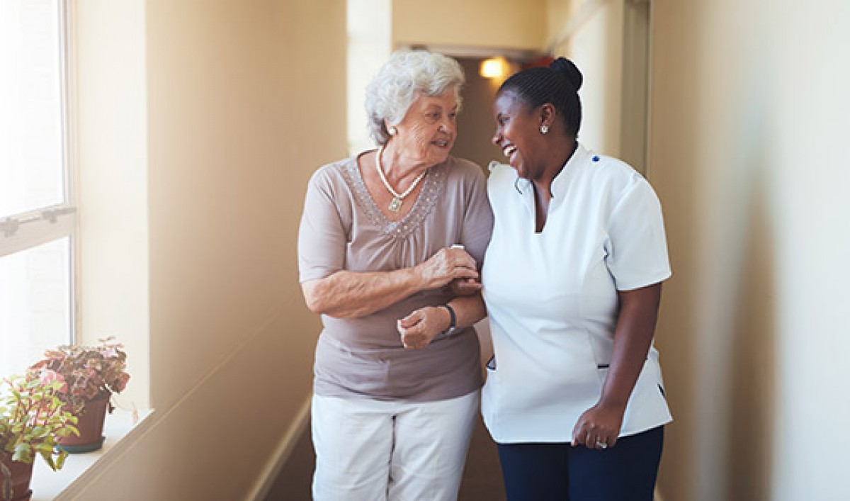 Elderly woman walking closely with nurse while laughing